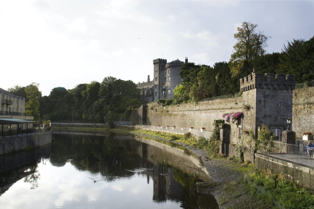 Stunning riverside view of scenic castle, lush greenery, and charming outdoor seating, inviting guests to relax and explore.