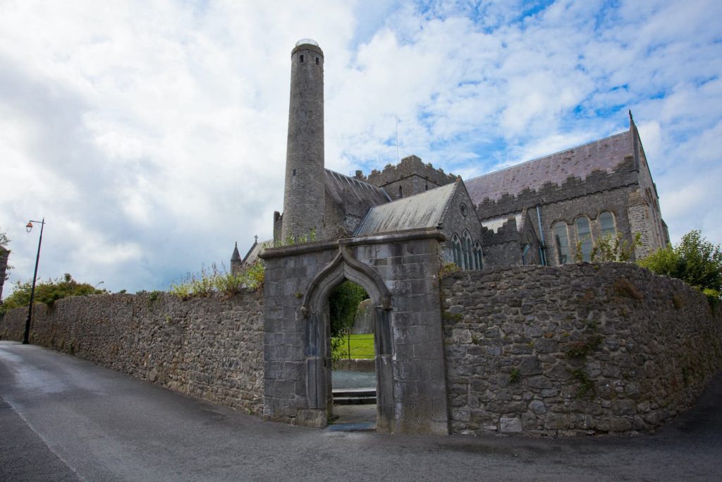 Charming stone church with a round tower, historic architecture, surrounded by a rustic wall, nestled under a bright sky.