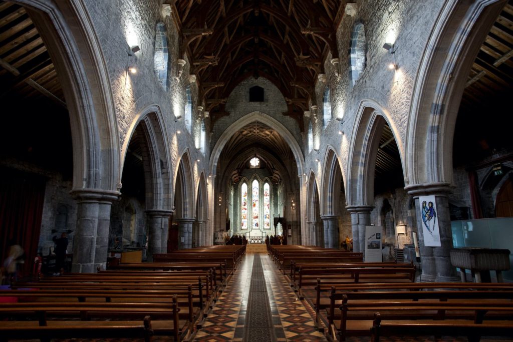 Historic church interior with stone arches, wooden pews, and stained glass window, offering a serene and spiritual ambiance.