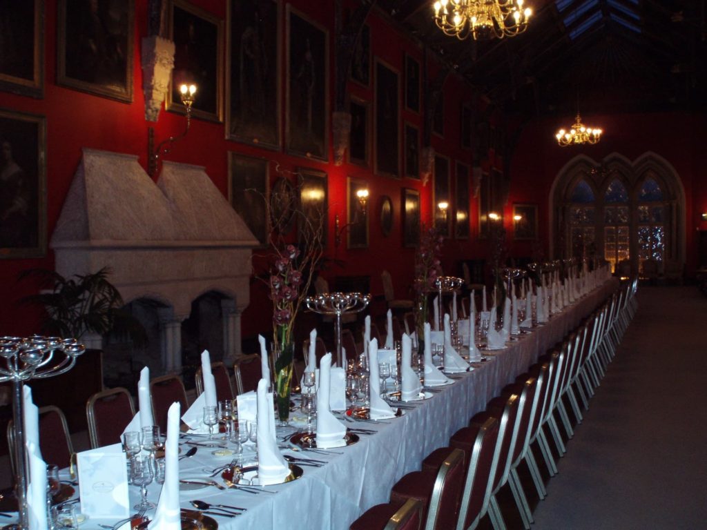 Elegant dining hall with long banquet table, classic chandeliers, and historic paintings in opulent hotel setting.