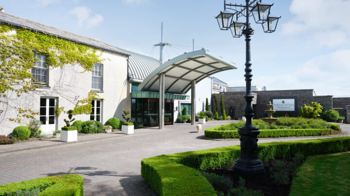 Elegant hotel entrance with manicured gardens, classic lamppost, and welcoming entrance canopy under a clear blue sky.