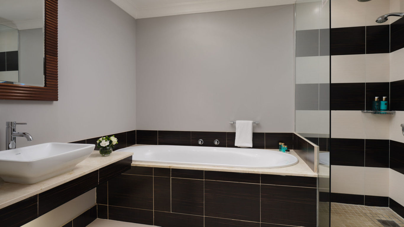 Luxurious hotel bathroom with modern fittings, spacious tub, sleek basin, glass shower, and elegant decor.