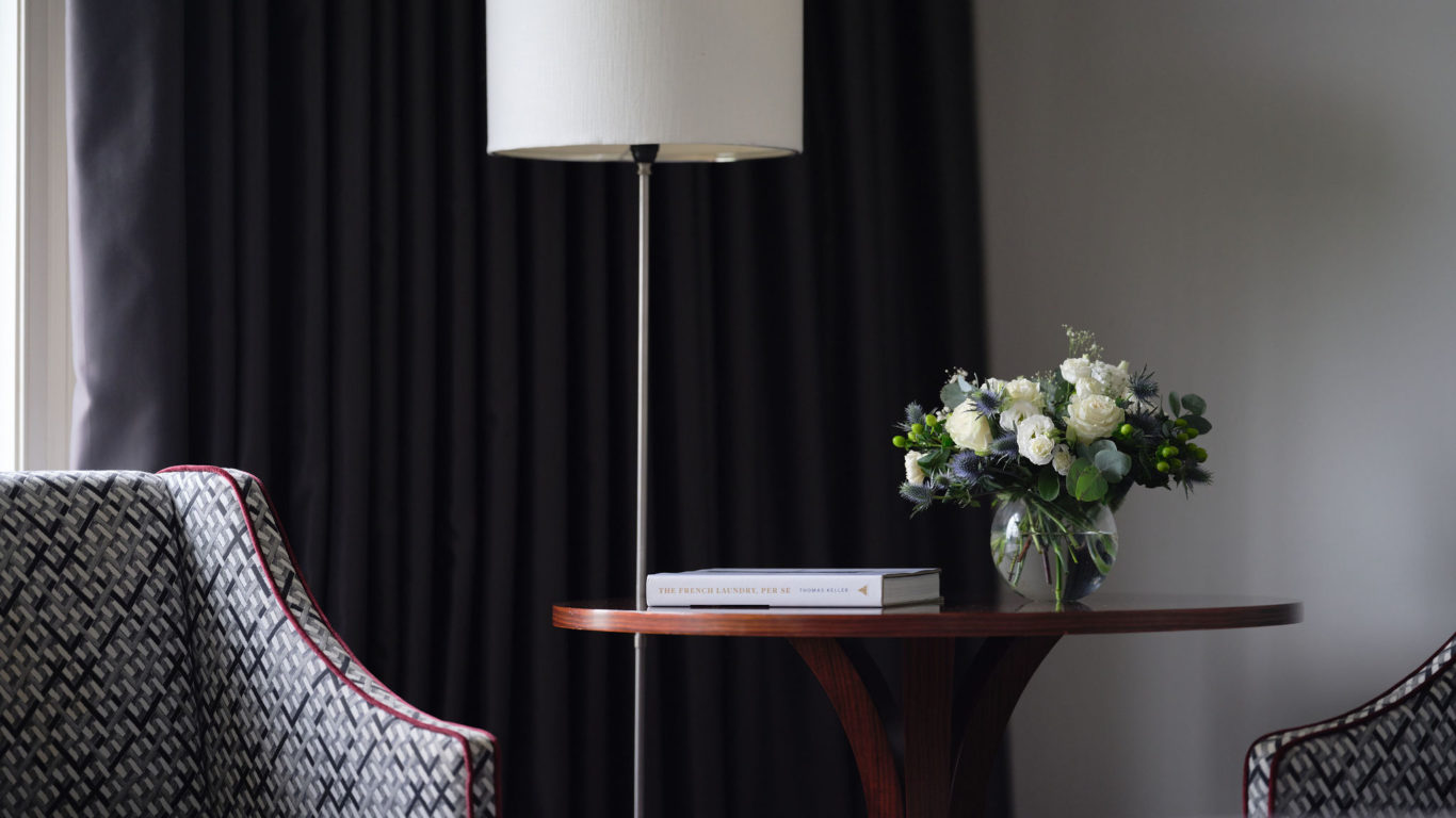 Elegant hotel lounge with cosy chairs, floral centrepiece, warm lighting, and sleek decor, offering a relaxing retreat.