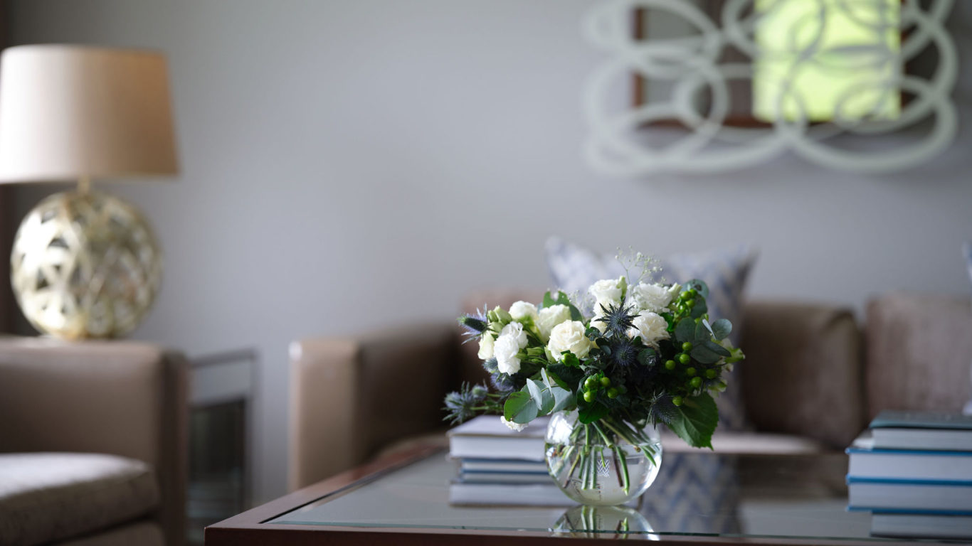 Elegant hotel lounge with plush sofa, floral display on glass table, and warm ambient lighting for relaxation.