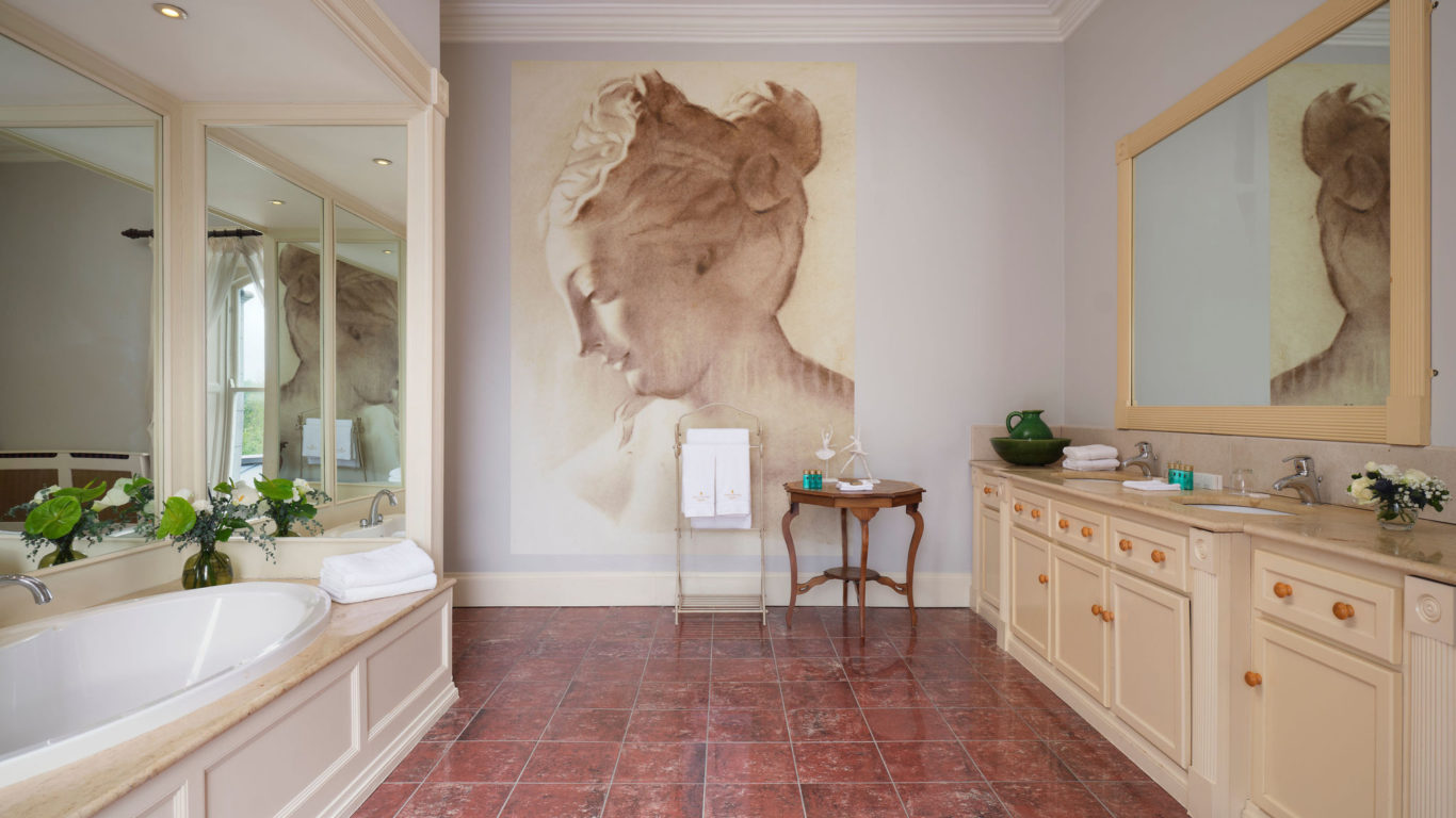 Elegant hotel bathroom with large mirrors, vintage painting, spacious tub, dual sinks, and plush towels for a relaxing stay.