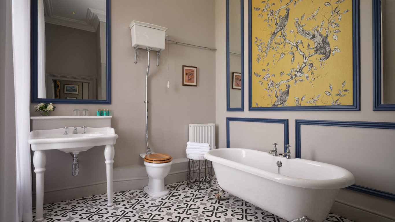 Elegant bathroom with clawfoot tub, ornate tile floor, large mirror, and artistic yellow wall mural, perfect for relaxation.
