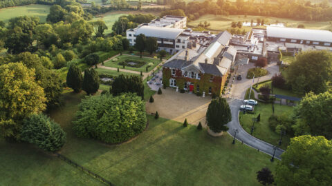 Aerial view of a charming country hotel surrounded by lush gardens, with spacious grounds and elegant architecture. Perfect retreat.