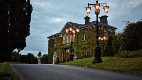 Elegant ivy-clad hotel exterior with vintage lamps illuminating a peaceful entrance. Lush gardens offer a serene welcome.