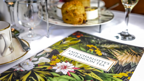 Elegant afternoon tea setup with scones, fine china, and a floral menu at a luxurious hotel, inviting a charming dining experience.