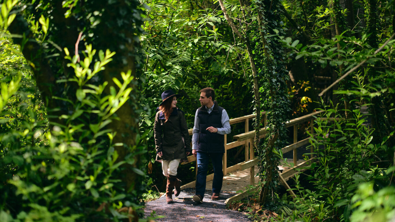 Guests stroll on a scenic forest trail with lush greenery and a wooden bridge, enjoying a nature retreat near the hotel.