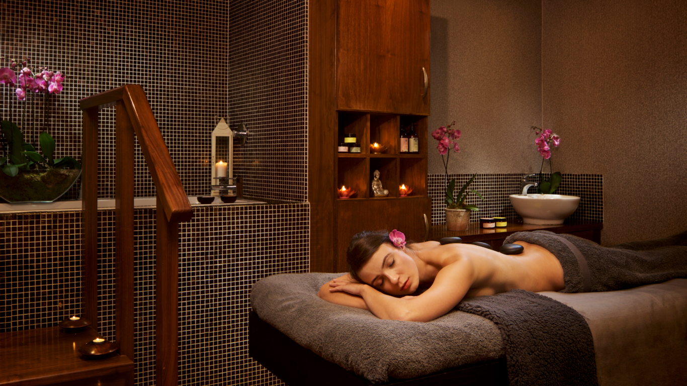Guest relaxing in tranquil spa room with candles, orchids, and soothing decor, experiencing a serene massage at luxury hotel.