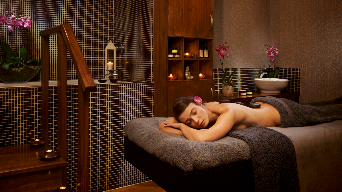 Guest relaxing in tranquil spa room with candles, orchids, and soothing decor, experiencing a serene massage at luxury hotel.