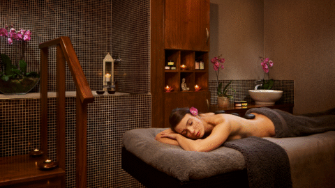 Relaxing spa treatment room with massage table, ambient lighting, candles, and fresh orchids for a tranquil hotel experience.