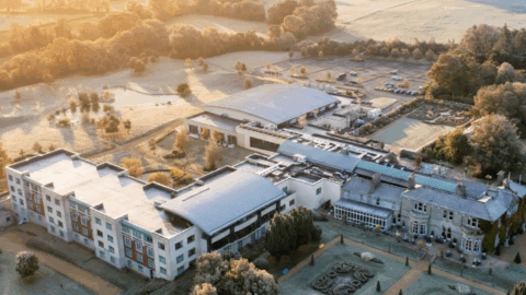 Aerial view of a large hotel complex surrounded by landscaped gardens and trees, with morning sunlight illuminating the scene.