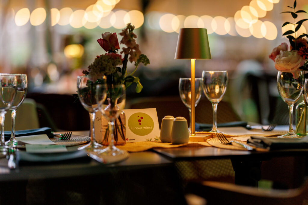 A decorated dining table with wine glasses, plates, a small lamp, flowers, and a 