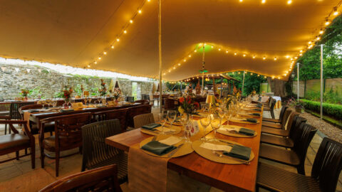 Elegant outdoor dining area with fairy lights, beautifully set tables, and garden views at luxury hotel.