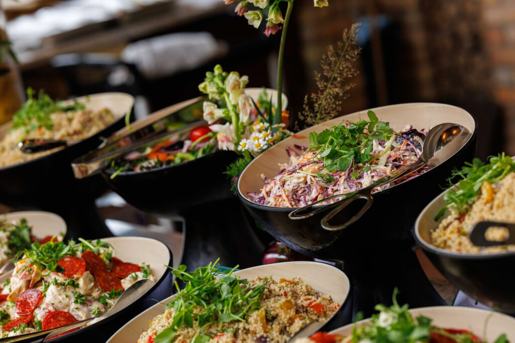 A buffet table with bowls of assorted salads, including coleslaw, grain salad, and dishes garnished with fresh greens and herbs.