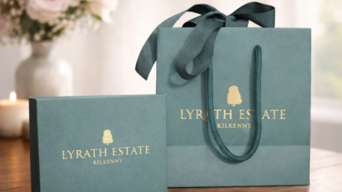 Elegant Lyrath Estate Kilkenny gift bag and box on wooden table with soft floral and candle background, inviting luxury.