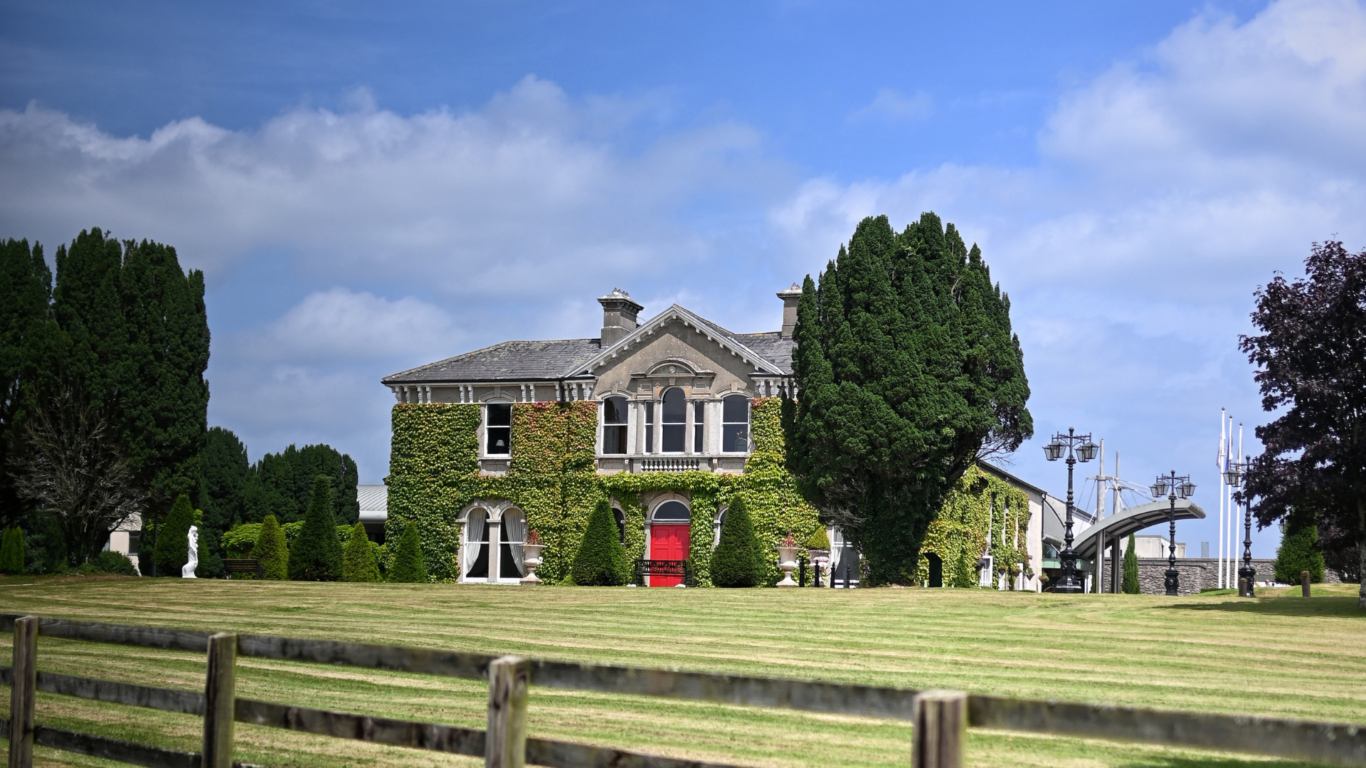 Charming countryside hotel with ivy-covered walls, lush gardens, and spacious grounds under a clear blue sky.
