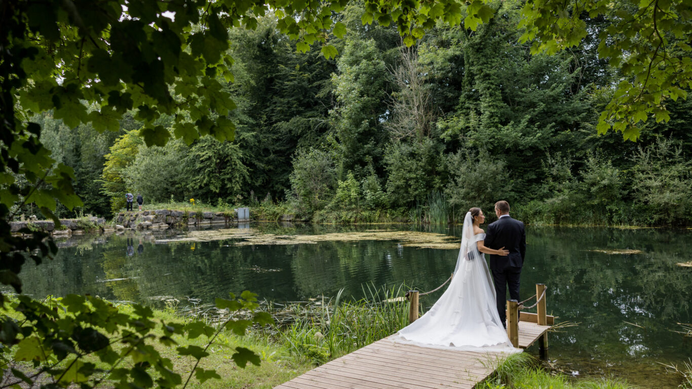 Couple on a romantic wooden dock overlooking serene lake surrounded by lush greenery, ideal for tranquil wedding stays.
