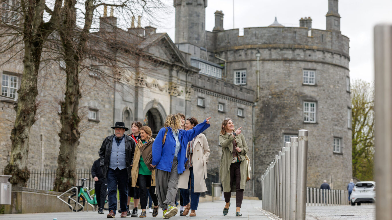 Guests enjoying a guided tour outside a historic stone castle, featuring charming architecture and lush surroundings.