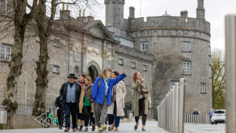 Guests enjoying a guided tour outside a historic stone castle, featuring charming architecture and lush surroundings.