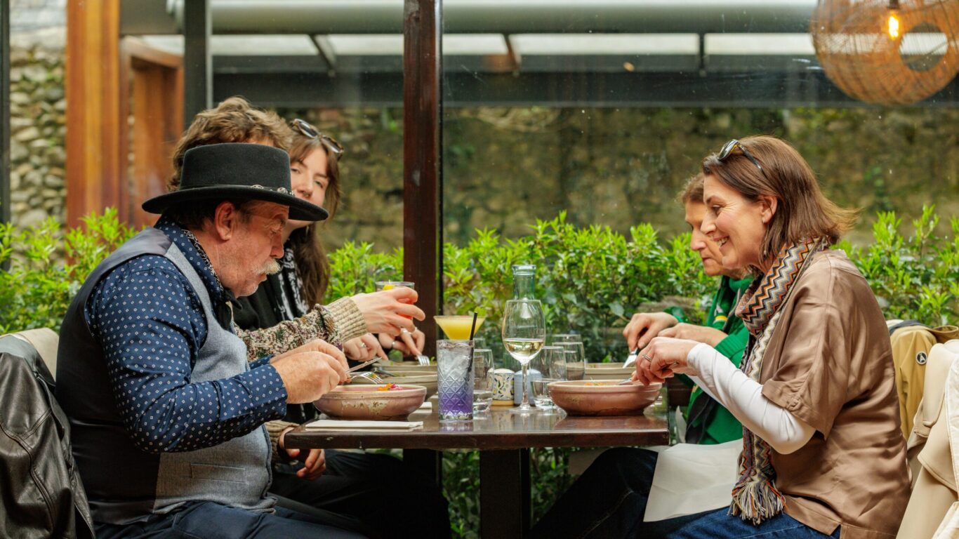 Guests enjoying a meal at an outdoor dining area with lush greenery, under warm lighting, at a stylish hotel restaurant.